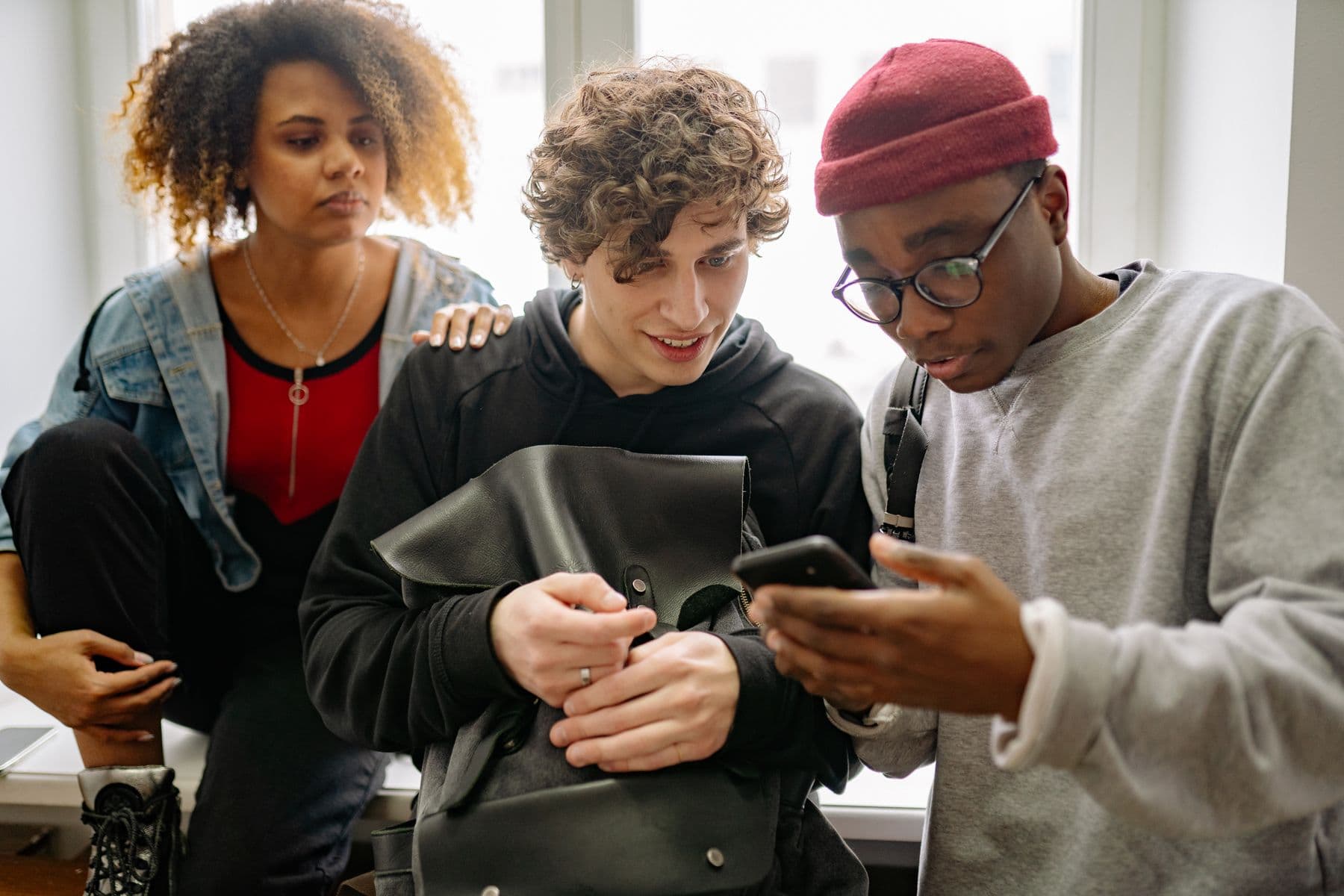 Three friends crowded around a phone, smiling at the contributions coming in