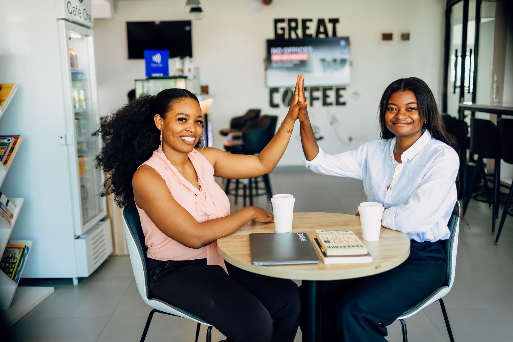 Two friends high-fiving over coffee at a café